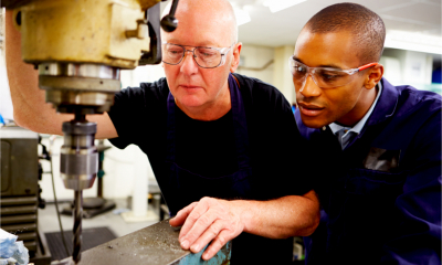An older man demonstrates a piece of equipment to an apprentice