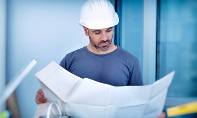 Worker in white hard-hat looking at big sheet of paper