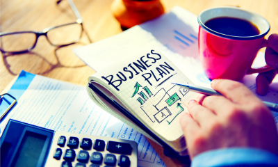 Man holding a coffee whilst writing his business plan to help him forecast cash flow and secure investments