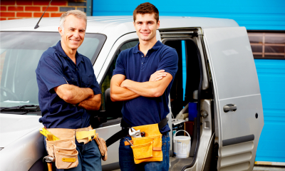 Two tradesman in blue tops stood beside a grey van