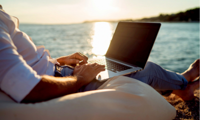 Man working on his laptop whilst sat on a beanbag at the beach on holiday