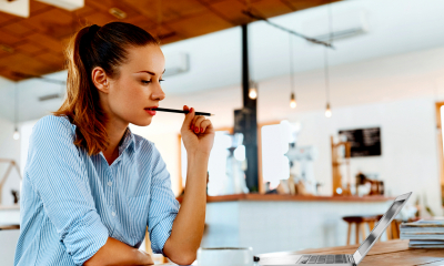 Female in blue shirt biting pencil considering freelance insurance