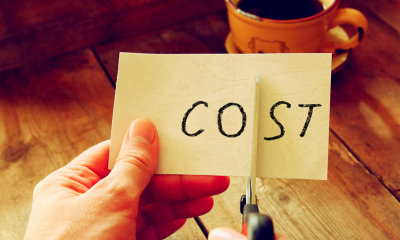 Cost control A man cuts a piece of paper with the word cost written on it