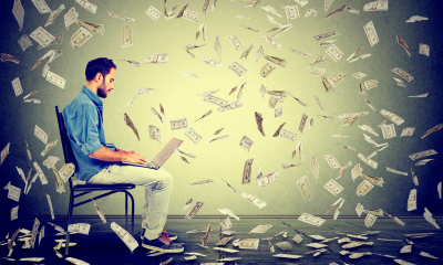 Man sat in a chair using his laptop with dollar bills falling around him
