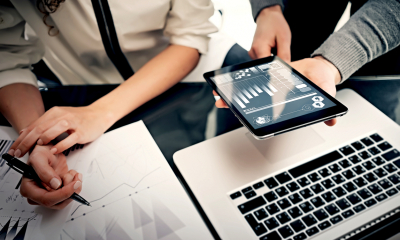 Hands holding tablet showing growth projections and working on papers with financial details