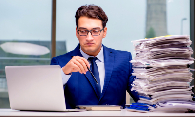 Man in a suit and glasses sat down with tax bills and a laptop at the desk