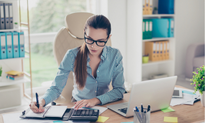 Portrait of serious young businesswoman accountant in formal wear and with pony tale, sitting at her work place and doing notes