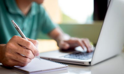 Getting a grant - checklist person on desk, with laptop and writing on notepad