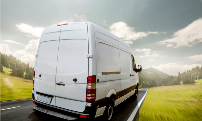 White transit van carrying goods through a grassy valley on a sunny day