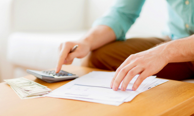 Man in a blue shirt calculating his tax with a stack of money beside him