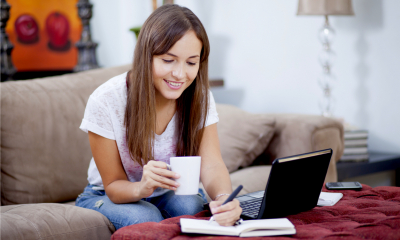 Woman sat on a sofa holding a mug while completing her home business insurance
