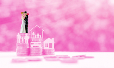 Miniature couple on steps of rising coins on pink background, depicts tax savings for married couples