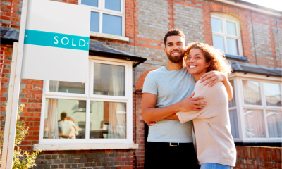 Portrait of excited couple standing outside new home with sold sign