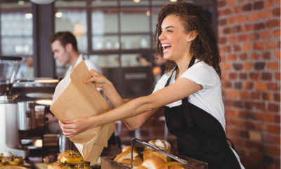 Laughing barista giving paper bag to customer at coffee shop
